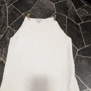 Vit linnetopp med guldkedjor från Amisu xs - Snygg vit linnetopp från Amisu med trendiga axelband i guldfärgad kedja. Toppen har en rak, enkel passform och är perfekt för dig som gillar stilrena plagg med en twist. Materialet känns mjukt och lätt, vilket gör den skön att bära under varma dagar.