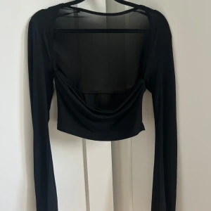 Svart mesh croppad topp  - Svart croppad topp med långa, ”häxiga” ärmar i mesh. Ungefär som en tubtopp med ärmar, framtill, men med mer stängd rygg. Toppen är figurnära och har en svart rygg med transparenta meshdetaljer. Är numera strl. M så rekommenderar att du är xs-s om du har denna, samt skippar bh:n.