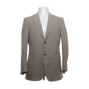 Beige randig kavaj Tiger of Sweden - Snygg beige kavaj från Tiger of Sweden med tunna vita ränder. Klassisk modell med två knappar framtill, fickor med lock och smal krage. Tillverkad i 100% bomull med viskosfoder. Perfekt för en stilren look.