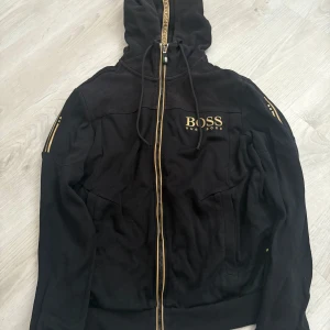 Svart zip-hoodie från Hugo Boss -  Äkta Svart zip hoodie med guld detaljer från Hugo Boss i storlek S pris kan diskuteras