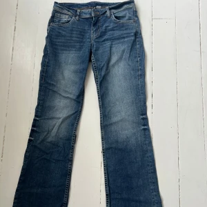 Blå lågmidjade bootcut jeans med slitningar - Snygga blå jeans med bootcut passform och lätt slitna detaljer framtill och och bak. Jeansen har en något ljusare tvätt på låren och baksidan.  Är i stl 40 men mer som en 38