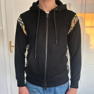 Svart Burberry hoodie med rutiga detaljer - Säljer en svart hoodie från Burberry i storlek S. Endast använd fåtal gånger så i väldigt bra skick. 