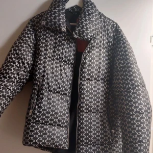 Svartvit pufferjacka med mönster - Snygg pufferjacka i svart med vitt rutigt mönster. Jackan har hög krage, dragkedja framtill och två fickor med dragkedja. Perfekt för kalla dagar och ger en cool vibe till din outfit.