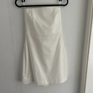 Vit axelbandslös kort klänning S - Snygg vit axelbandslös kort klänning i stilren design. Klänningen har en figurnära passform och är perfekt för dig som gillar att klä sig elegant. Helt oanvänd med prislapp kvar
