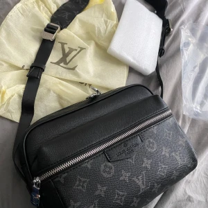 Svart Axel väska - Snygg svart axelväska från Louis Vuitton med klassiskt monogrammönster i grått. Väskan har justerbar axelrem med logga, silverfärgade metalldetaljer och dragkedja framtill. Tillverkad i tåligt skinnliknande material, perfekt för dig som vill ha en stilren och lyxig look.priset är absolut inte satt i sten 🙌🏽 