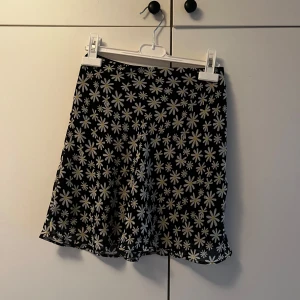 Blommig kortkjol från H&M Divided - Supersöt svart kortkjol från H&M Divided med vita och gula blommor över hela tyget. Kjolen har dragkedja och knapp i sidan för enkel påklädning. 