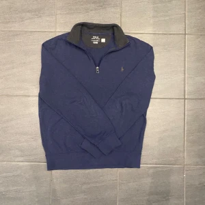 Blå half zip tröja från Polo Ralph Lauren - Mörkblå långärmad tröja från Polo Ralph Lauren med klassisk broderad logga på bröstet. Tröjan har en hög krage med half zip-dragkedja och är tillverkad i mjuk bomullsmix. Perfekt för lager-på-lager och chill stil.