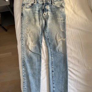 Ljusblå slitna jeans 1964 - Säljer ett par ljusblå jeans från 1964 med snygga slitningar och distressed detaljer framtill. Jeansen har klassisk femficksdesign, raka ben och normal passform. Perfekta för en avslappnad och trendig look.