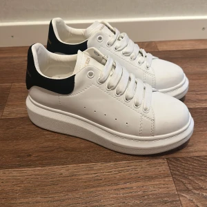 Alex McQueen vita sneakers - Snygga vita oäkta sneakers från Alex McQueen med svart hälparti och guldfärgad logga. Skorna har chunky platt sula, rund tå och klassisk snörning. Behövs torkas av men kommer tvätta av dem så gott jag kan innan jag skickar