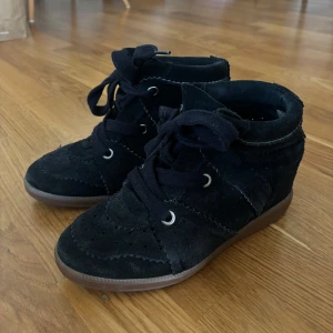 Svarta kilklackade boots Isabel Marant - Snygga svarta boots från Isabel Marant i mocka med kilklack och snörning. Skorna har rund tå, dekorativa sömmar och perforerade detaljer. Yttersulan är i gummi och ger bra grepp. Perfekta för dig som vill ha både stil och komfort.