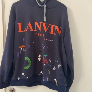 Lanvin x Gallery Dept. hoodie, marinblå - Snygg marinblå hoodie från Lanvin x Gallery Dept. med stor röd logga på framsidan och coola färgstänk i grönt, lila, vitt och gult. Grå snörning i huvan och broderad detalj på axeln. Mjuk bomullskänsla och relaxed fit. Bak finns diskret tryck med Gallery Dept. Storlek M känns som L, Pris går att diskuteras