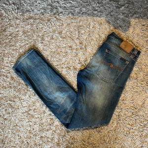 Blå jeans från Nudie Jeans, W30 L32 - Säljer ett par klassiska blå jeans från Nudie Jeans med snygg slitning och kontrastsömmar. Modellen har raka ben, fem fickor och ikonisk broderad bakficka. Perfekta för dig som gillar en avslappnad men stilren look. Storlek w30 men mått kan såklart skickas vid osäkerhet, postas antigen samma dag som köp eller dagen därpå🙌💯