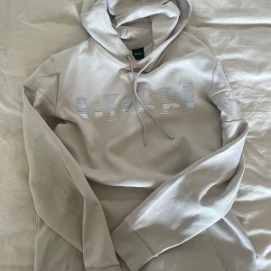 Huvtröja Hugo Boss - Huvtröja från Hugo Boss i krämvit med silvertext i storlek M. 