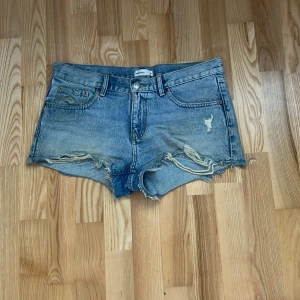 Blå jeansshorts med slitna detaljer - Snygga blå jeansshorts från Gina Tricot med råa, fransiga kanter och slitningar framtill. Klassisk femficksmodell med knapp och dragkedja. Perfekta för varma dagar och en avslappnad look.