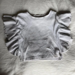 Vit volangärmad topp från Zara - Superfin vit topp från Zara med breda volangärmar och öppen rygg. Ribbad struktur i tyget och croppad passform som ger en trendig look..