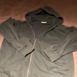 Mörkgrön hoodie från Weekday - Säljer en mörkgrön hoodie från Weekday med dragkedja och huva. Hoodien är normal fit och passar väldigt snyggt med en overshirt eller en T-shirt under. Skriv om du har några frågor.