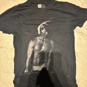 Svart tupac t-shirt - Säljer en svart t-shirt tupac T-shirt. Skit snygg och passar perfekt för dig som gillar tupac eller y2k stil. Skriv om du har några frågor