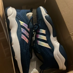 Blå Adidas Haiwee J sneakers - Snygga blå Adidas Haiwee J sneakers med ett unikt mönster på de ikoniska tre ränderna. Skorna har en modern design med en bekväm sula och snörning. Perfekta för en sportig look.