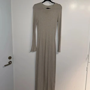 Beige glittrig långklänning från Gina Tricot - Snygg beige långklänning från Gina Tricot med glittrande detaljer. Klänningen har en tight passform och långa ärmar, perfekt för en elegant look. Den är tillverkad i ett bekvämt material som ger en fin siluett.