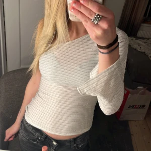 Vit glittrig oneshoulder topp - Säljer en snygg vit glittrig oneshoulder topp med lång ärm. Perfekt för en kväll ute eller en festlig tillställning. Liten i storleken