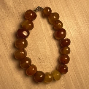 Brunt armband med stora pärlor - Snyggt armband med stora, glansiga pärlor i olika nyanser av brunt. Perfekt för att ge en naturlig touch till din stil. Armbandet har en enkel låsning som gör det lätt att ta på och av.