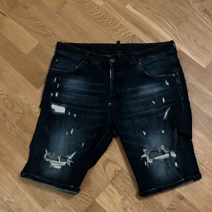 Svarta jeansshorts från Dsquared2 - Snygga svarta jeansshorts från Dsquared2 med slitna detaljer och en cool look. De har en knapp och dragkedja framtill samt klassiska fem fickor. Perfekta för en avslappnad stil. Knappt använda och passar inte mig.