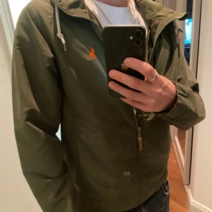 Grön jacka från Ralph Lauren windbreaker - Säljer en snygg grön jacka från Ralph Lauren med dragkedja och huva. Storlek Xs men passar även S. Jackan har en broderad logga på bröstet och snörning vid huvan. Perfekt för en stilren look. Den är i väldigt bra skick och givetvis äkta, skriv för fler bilder👍