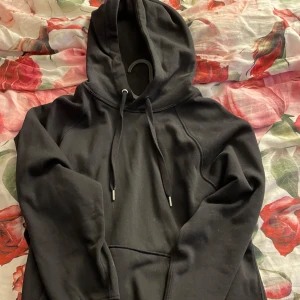 Svart hoodie från H&M Divided - Säljer en klassisk svart hoodie från H&M Divided. Den har en huva och en stor ficka framtill. Perfekt för en avslappnad stil. Använd Max 2 gånger.