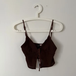 Brun ribbad linnetopp - Säljer en brun ribbad linnetopp med smala axelband och knytning framtill. Perfekt för varma dagar eller som ett lager under en jacka. Enkel och stilren design som passar till mycket.