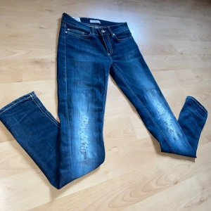 Blå jeans från Dondup (Helt nya) - Snygga blå jeans från Dondup med slitna detaljer och klassisk femficksdesign. De har en knappgylf och kontrasterande sömmar som ger en cool look. Perfekta för en avslappnad stil. W28 L30/31