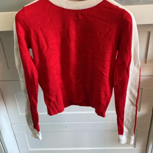 Röd och vit tröja - Snygg röd tröja med vita detaljer längs ärmarna. Perfekt för en färgglad look. Tröjan har långa ärmar och en bekväm passform.
