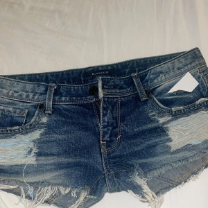 Blå jeansshorts från blueskin  - Snygga blå jeansshorts från Blueskin med slitna detaljer och fransar. Perfekta för en avslappnad stil. De har en klassisk femficksdesign och knappgylf. Köpta second hand i Thailand så är ej säker på storlek men skulle säga 34, midjemåttet är 40cm rakt över💖