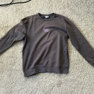 Grå sweatshirt från H&M med lila tryck - Säljer en grå sweatshirt från H&M med ett lila tryck på baksidan. Tröjan har långa ärmar och en rund halsringning. Använder den inte längre men den är i bra skick. Motivet på baksidan är lite slitet men it så farligt mycket.