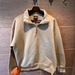 Mint tröja med dragkedja från H&M - Säljer en stilren grå tröja från H&M med halv dragkedja och relaxed fit. Perfekt för en avslappnad look. Tröjan har långa ärmar och ribbade muddar vid ärmslut och nederkant.