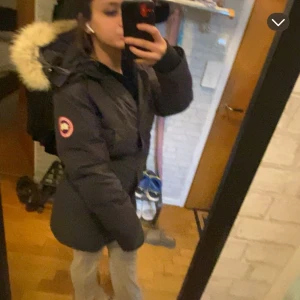 Svart parkajacka med pälsdetalj - Säljer en svart parkajacka från Canada Goose med pälsdetalj på huvan. Jackan har en klassisk design med lång ärm och en logotyp på ärmen. Perfekt för kalla dagar. Pris kan såklart diskuteras. Hör av er🫶🏻