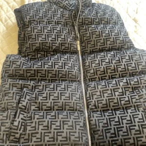 Svart och grå dunväst från Fendi - Snygg dunväst från Fendi i svart och grått med ett iögonfallande mönster. Västen har en dragkedja framtill och praktiska fickor. Perfekt för att hålla sig varm och stilren.