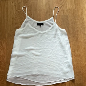 Vit linnetopp från Selected Femme - Säljer en stilren vit linnetopp från Selected Femme. Toppen har tunna axelband och en luftig passform, perfekt för varma dagar. Den är tillverkad i ett lätt och bekvämt material som ger en avslappnad look. Passar bra till både jeans och kjol.