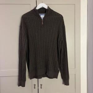 Brun stickad halfzip från Lindbergh - Säljer en stilren brun stickad tröja från lindbergh med dragkedja vid halsen. Tröjan har ett klassiskt flätmönster och långa ärmar, perfekt för kyligare dagar.
