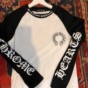  Chrome Hearts tröja  - Säljer en svartvit långärmad tröja från Chrome Hearts. Tröjan har ett stort tryck på ärmarna och bröstet med märkets logotyp. Storlek M. Vet ej om den är äkta