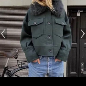 Mörkgrön jacka med fuskpäls - Snygg mörkgrön jacka med fuskpäls på kragen. Jackan har en croppad passform och knappar framtill. Perfekt för kyligare dagar med sina långa ärmar och stilrena design. Pris kan diskuteras!