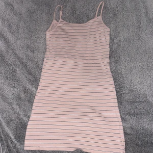 Rosa randig klänning - Säljer en söt rosa klänning med smala axelband och ett randigt mönster. Perfekt för varma dagar och kan enkelt stylas med en jeansjacka eller sneakers. Klänningen har en bekväm passform och är gjord i ett mjukt material.