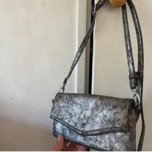 Silvrig axelremsväska  - Silvrig axelremsväska som går att justera banden, köpt second hand så vet ej vart ifrån, använt fåtal gånger så kan finnas tecken på slitage💞
