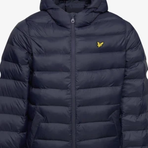 Mörkblå dunjacka från Lyle & Scott - Säljer en snygg mörkblå tunn dunjacka från Lyle & Scott med dragkedja och deras ikoniska logga på bröstet. Jackan har långa ärmar och är perfekt för vårens dagar. Den är både stilren och funktionell.