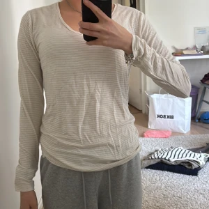 Vit randig långärmad tröja - Säljer en vit långärmad tröja med tunna och guld ränder. Tröjan har en normal passform.