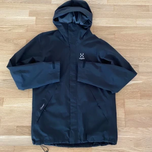 Haglöfs jacka  - Haglöfs Tjärn jacka i färgen true black. Jackan är i nyskick då den bara är använd ett fåtal gånger. Perfekt vår och höst-jacka som för övrigt är vattenavvisande. Nypris på denna goding är ca 1400 kr. 
