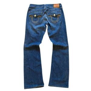 True Religion jeans bootcut flared low waist - Snygga blå jeans från True Religion med klassisk femficksdesign och kontrasterande sömmar. De är lågmidjade och bootcut och är tillverkade i slitstarkt denim. Perfekta för en avslappnad look. Ytterben 98 cm, innerben 76 cm, midja 39 cm