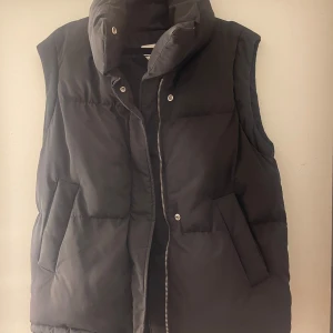 Svart dunväst med dragkedja - Snygg svart dunväst med dragkedja och knappar. Perfekt för vår och sommar dagar, är i väldigt fint skick. Köpare står för frakt.