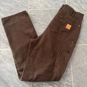 Carhartt Double Knee - Snygga bruna Carhartt Double Knee byxor med en avslappnad passform. Storlek 28/32 men sitter lite större i midjan. Knappt använda, säljs då de inte kommer till användning. Pris kan diskuteras 