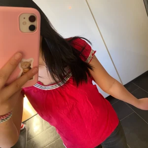 Röd topp med randiga detaljer från esprit - Säljer en röd topp med vita och svarta randiga detaljer vid hals och ärmar från märket esprit. Toppen har korta ärmar och två dekorativa knappar vid nederkanten. Perfekt för en färgglad look! Pris kan diskuteras 💕