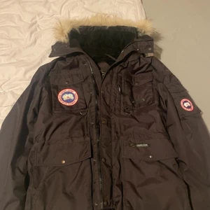 Canada goose jacka - Säljer en parkajacka från Canada Goose med pälsdetalj på huvan. Jackan har flera fickor med knappar och en dragkedja framtill. Insidan är quiltad för extra värme. Perfekt för kalla dagar!